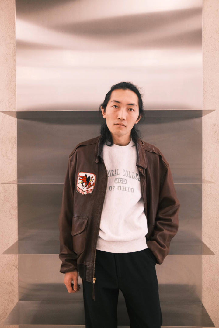 Person wearing a A2 brown jacket with a logo and a white shirt in an indoor setting