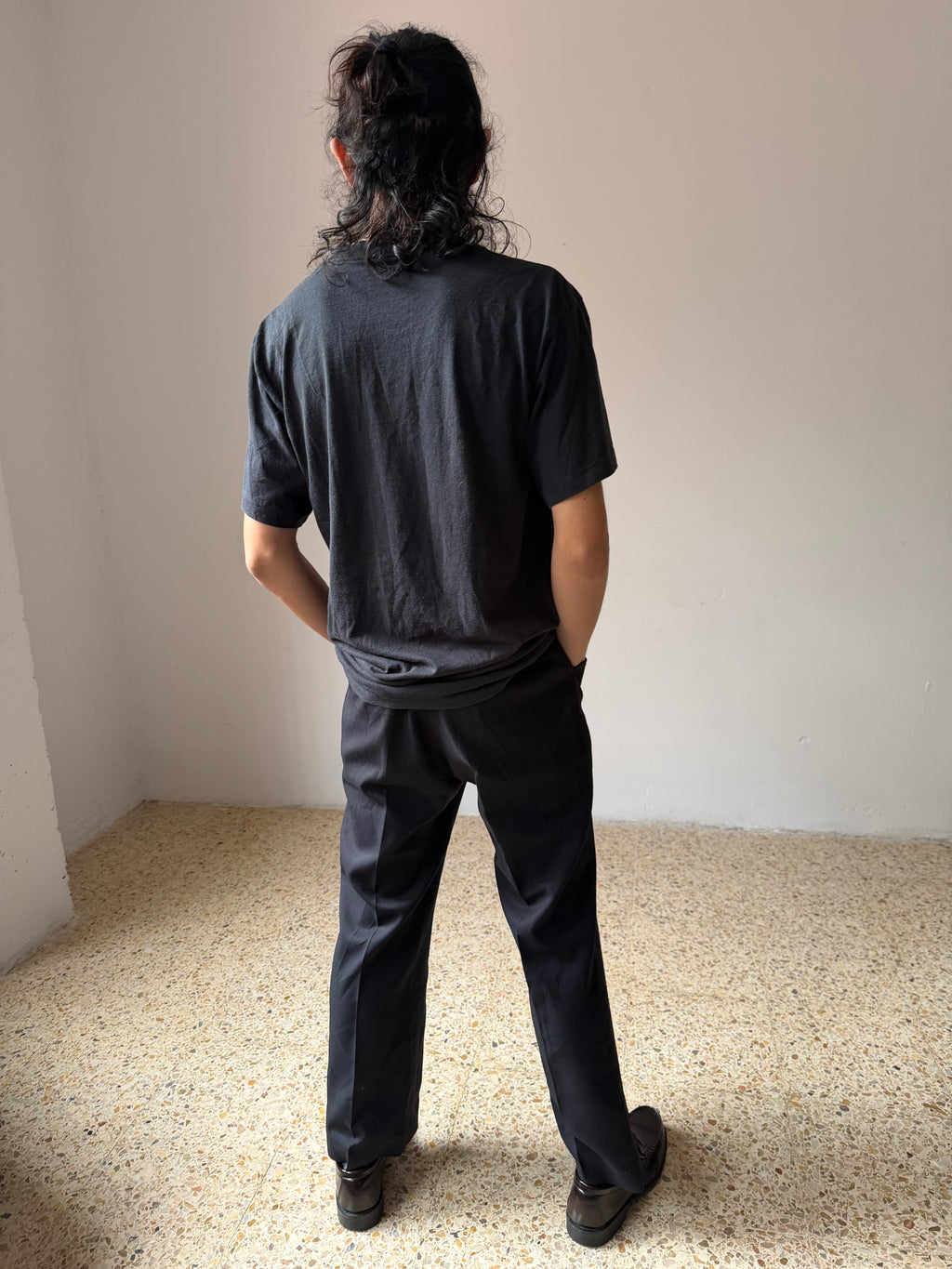 Person wearing a black Athletic Duke t-shirt and pants standing in a minimalistic room with light-colored floor and walls.