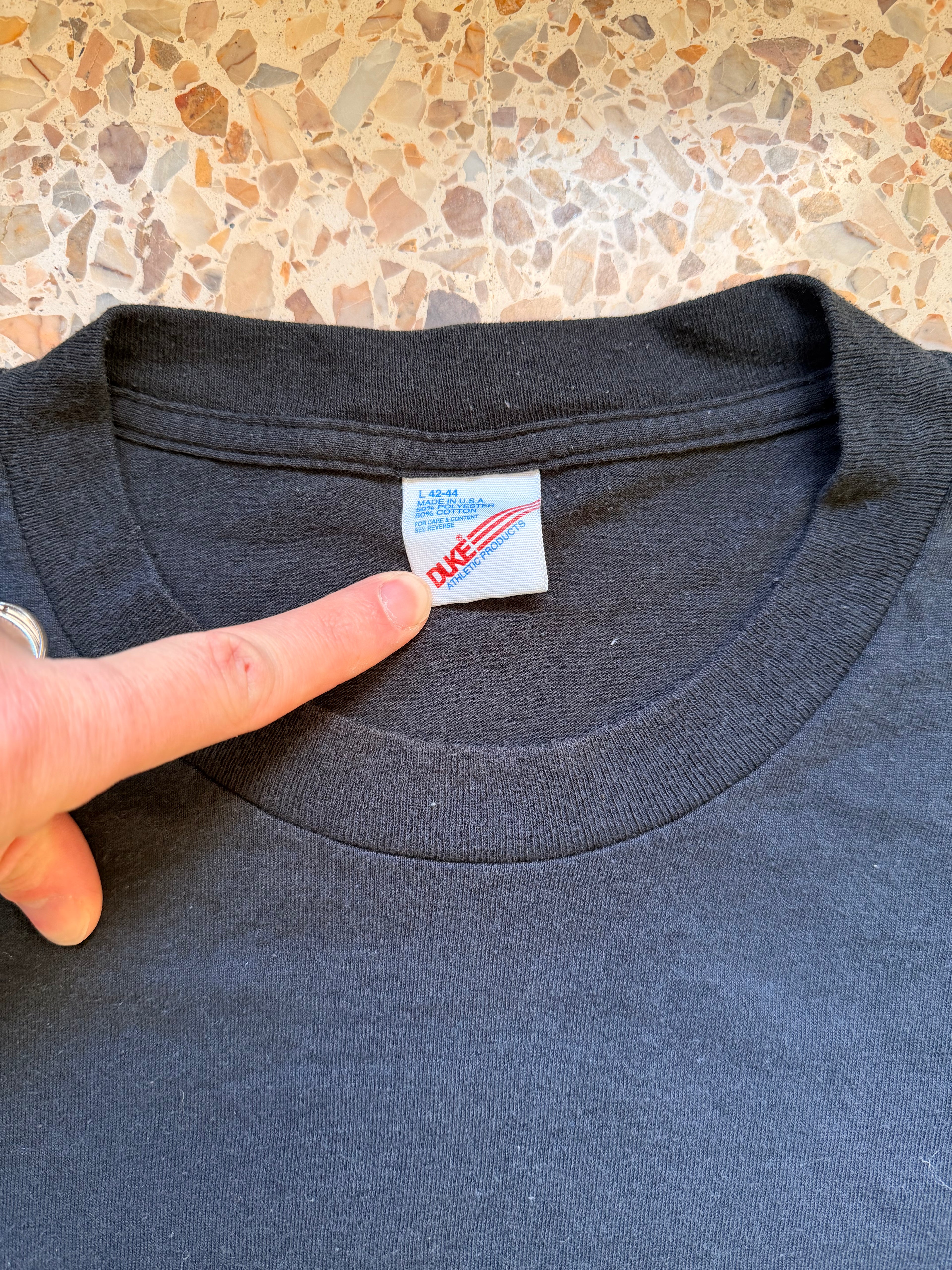 Close-up of a black tee with a label Duke Athletic product on a textured surface