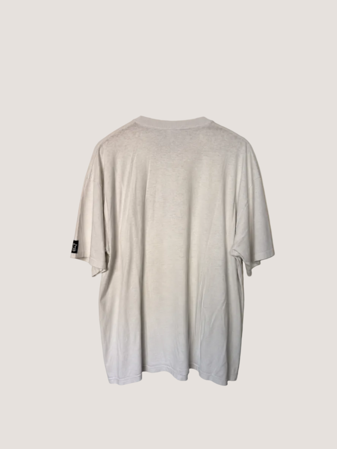 White t-shirt with a brand logo on the back, against a beige wall.