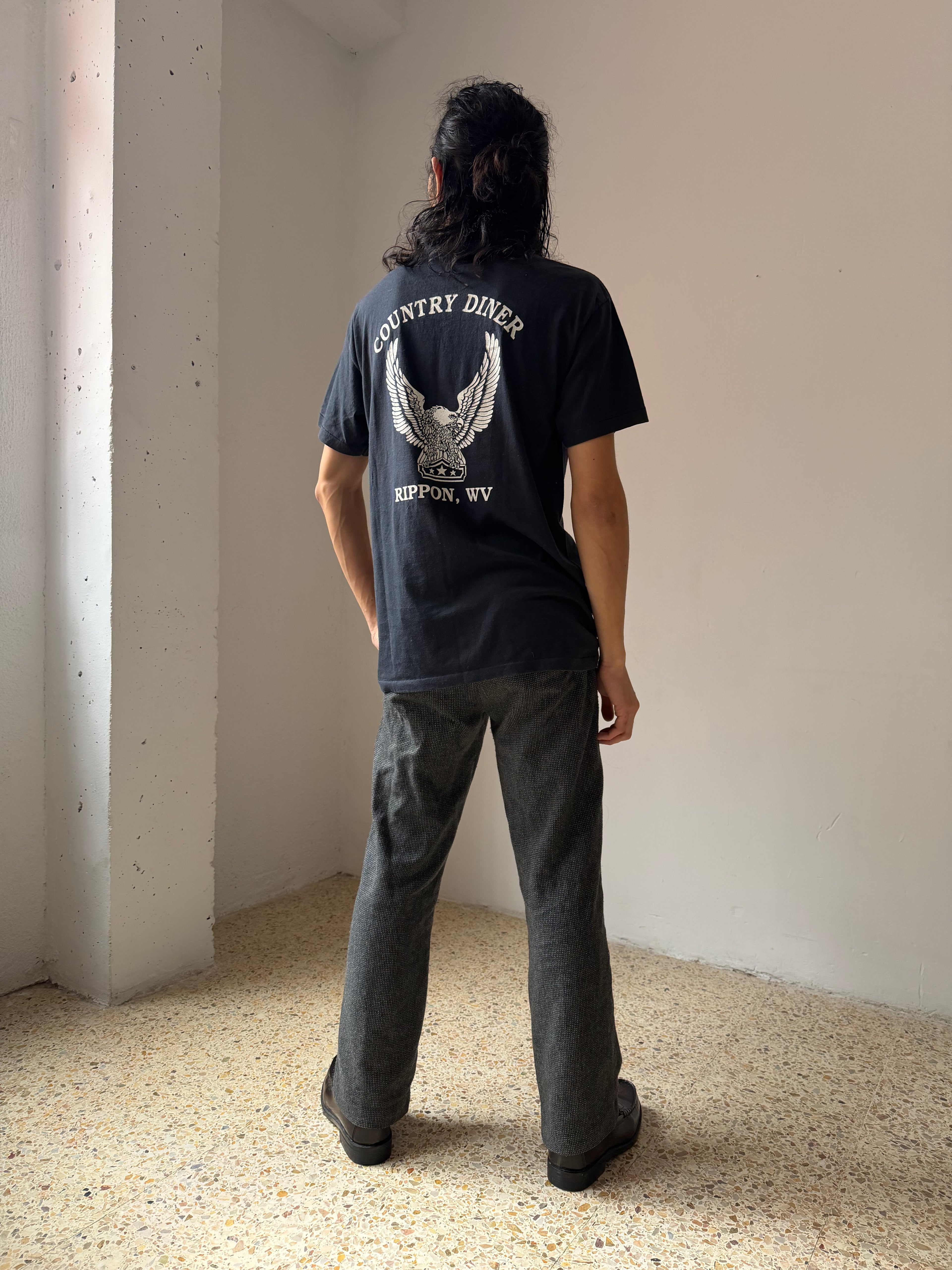Person wearing a black t-shirt with 'Country Diner' logo, standing in a minimalistic room.