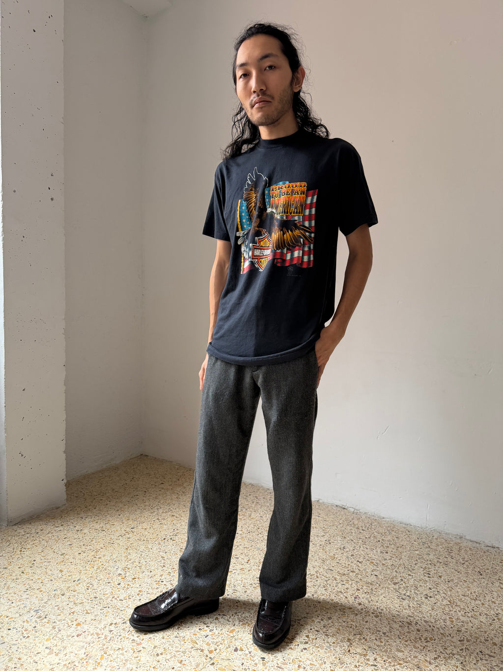 Person wearing a black Harley Davidson t-shirt with a colorful graphic design, standing in a minimalistic room.