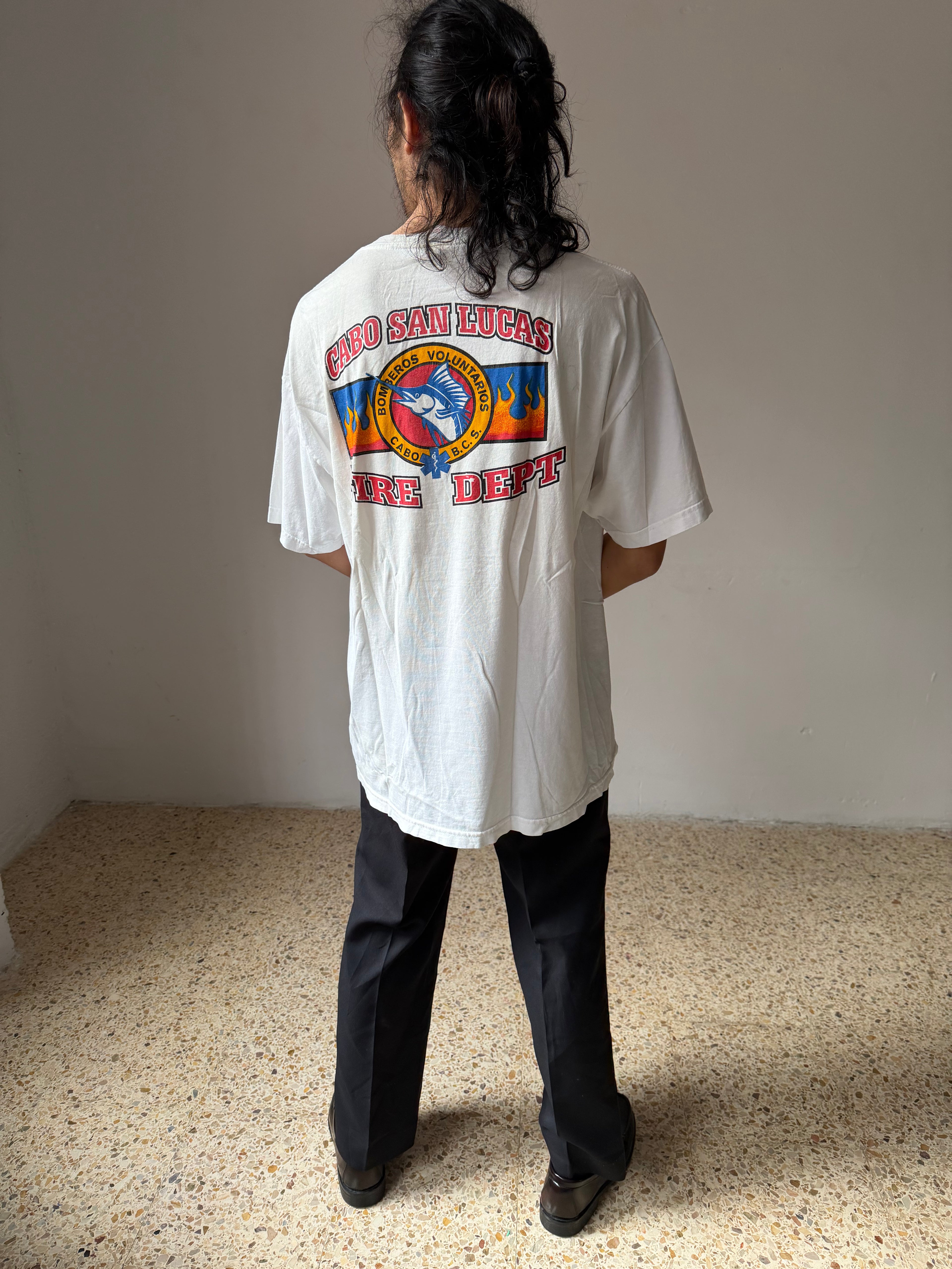 Person wearing a white t-shirt with colorful graphics and text, standing in a room with a plain background.