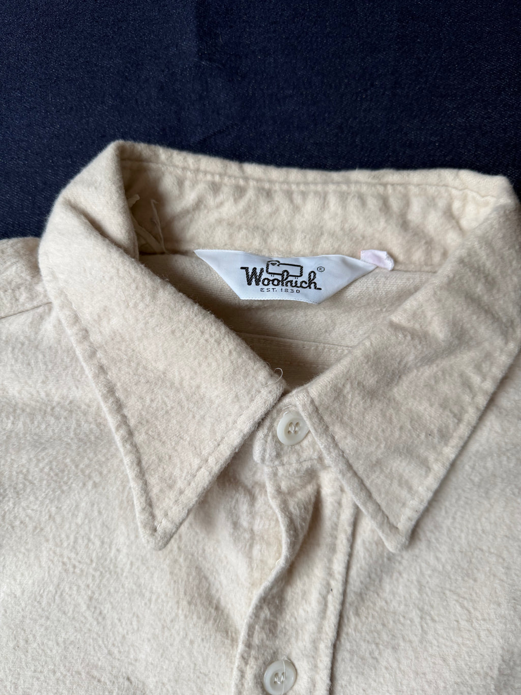Close-up of a beige shirt collar with a visible brand label against a dark background