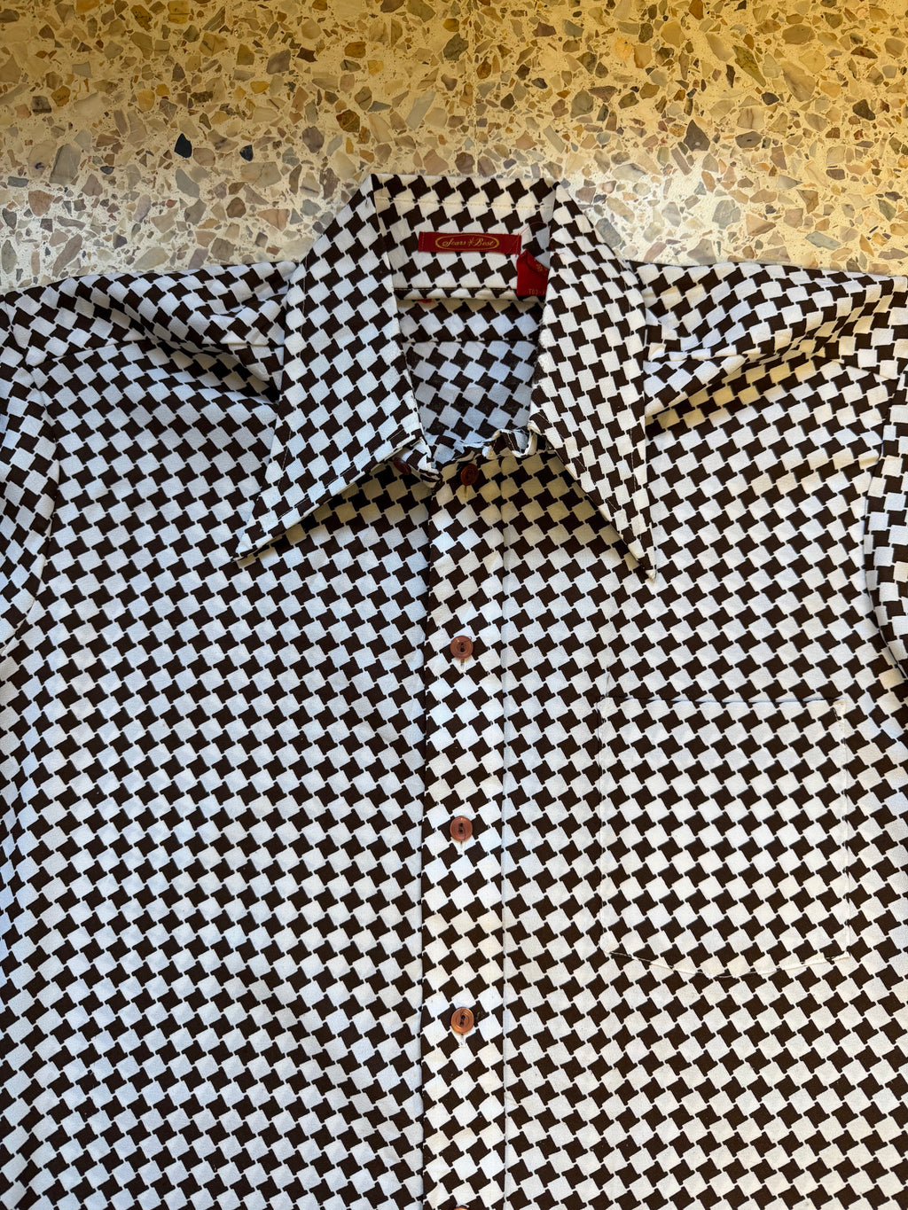 Close-up of a black and white checkered shirt with a red stripe on a textured surface.