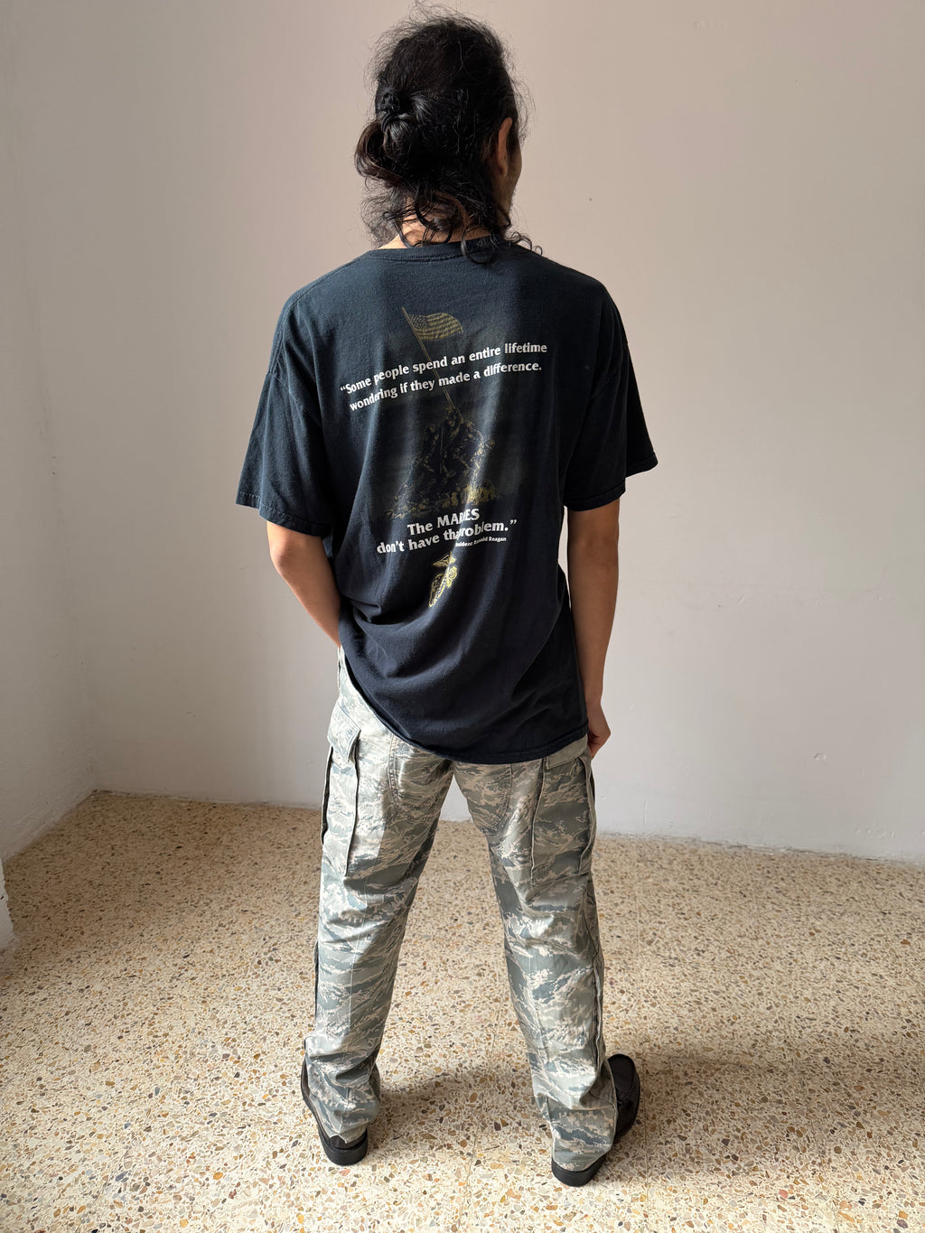 Person wearing a black Marines t-shirt with quotes and graphics, standing on a beige floor.
