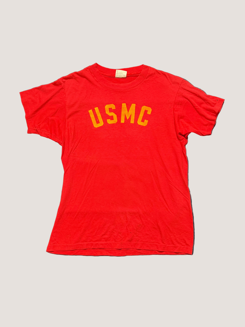 Red t-shirt with 'USMC' printed on it, laid flat on a gray surface