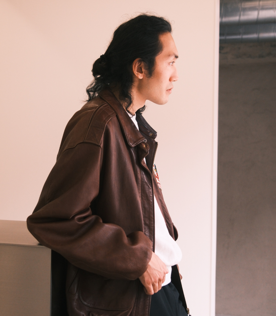 Man wearing a A2 brown leather jacket leaning against a wall.