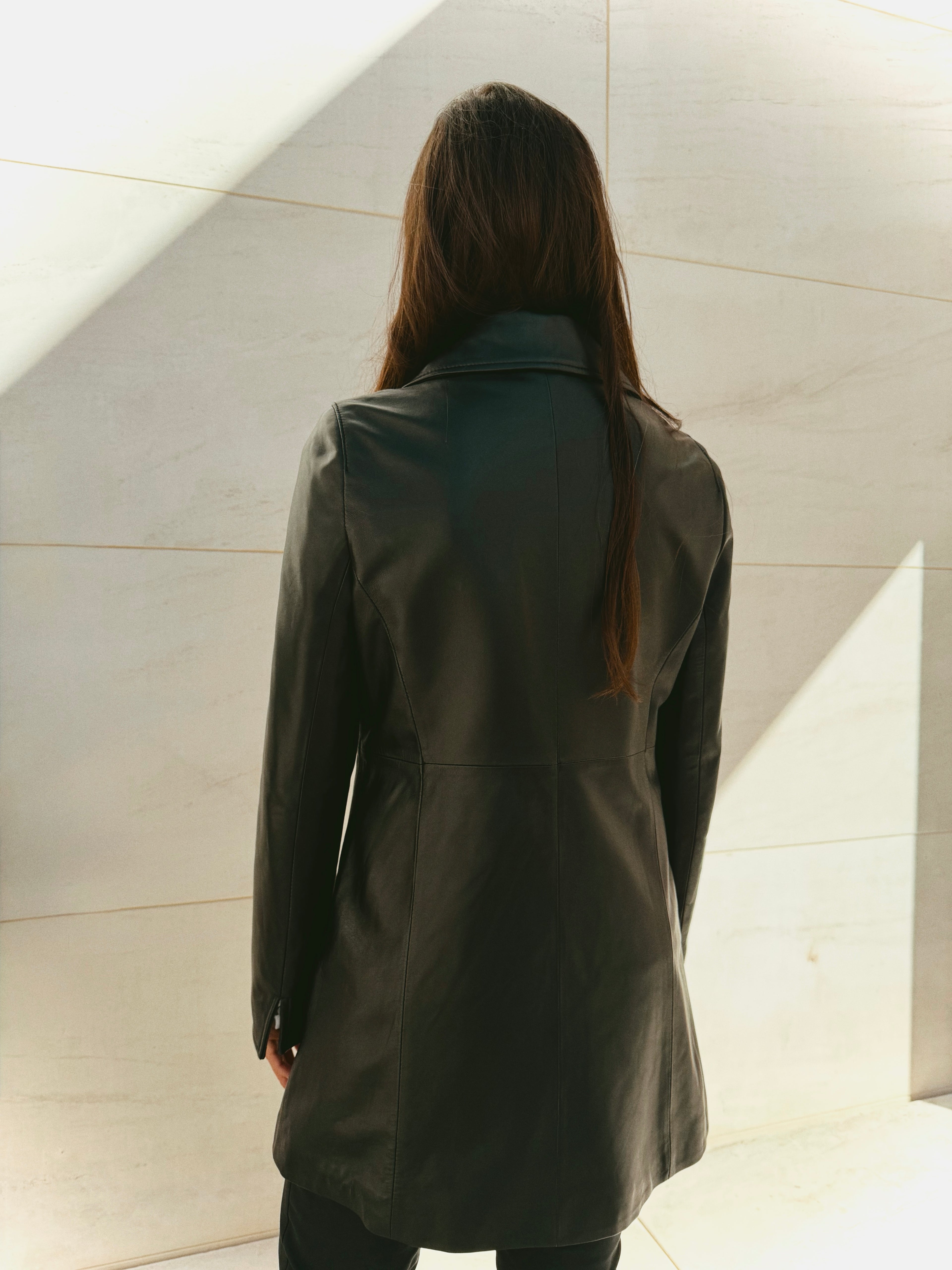 Woman wearing a Balmain black coat standing against a light-colored wall.