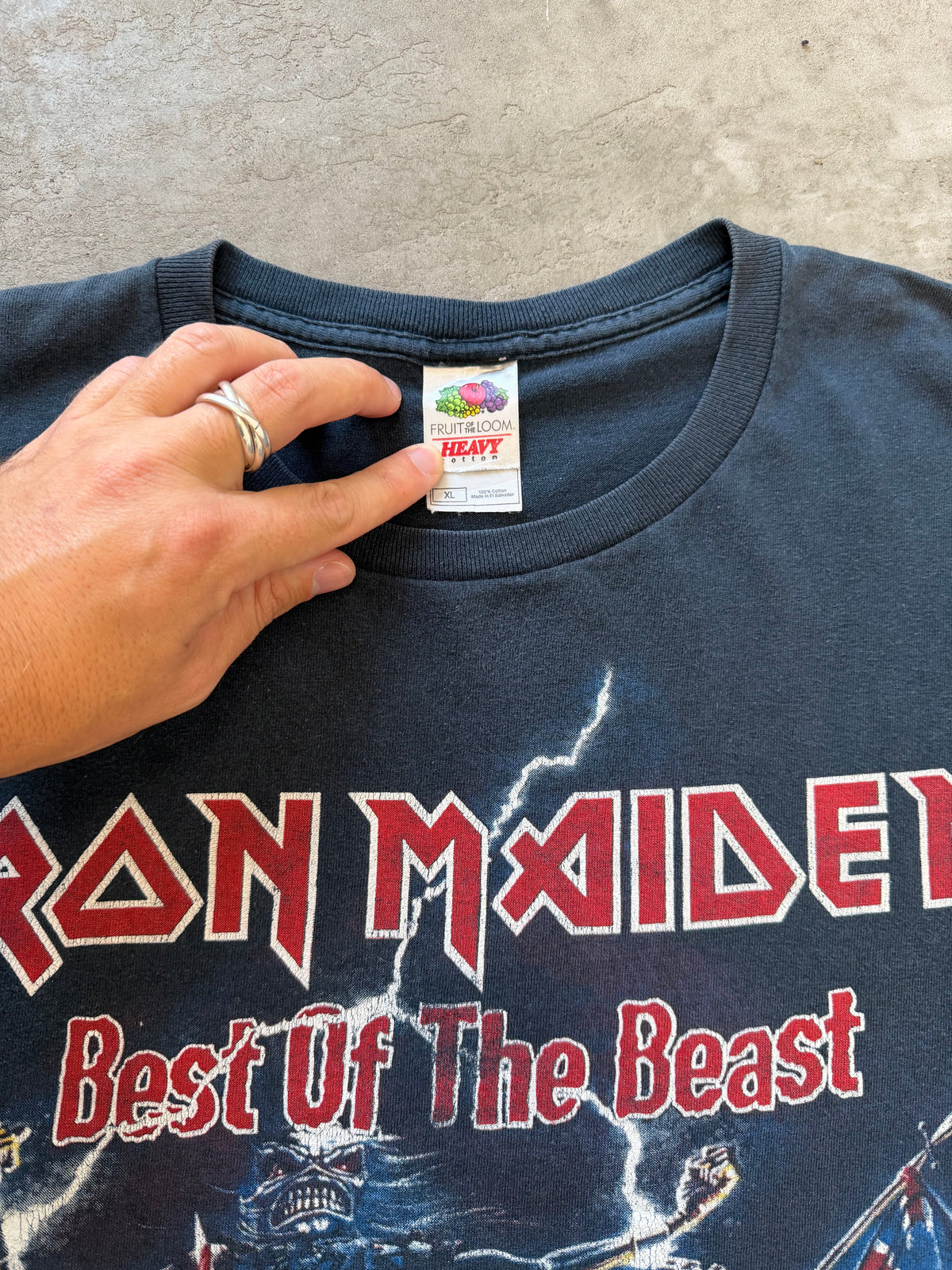 A close-up of a vintage Iron Maiden 'Best Of The Beast' t-shirt, showing the front graphic and a hand pointing to the neck label which reads 'HEAVY'.
