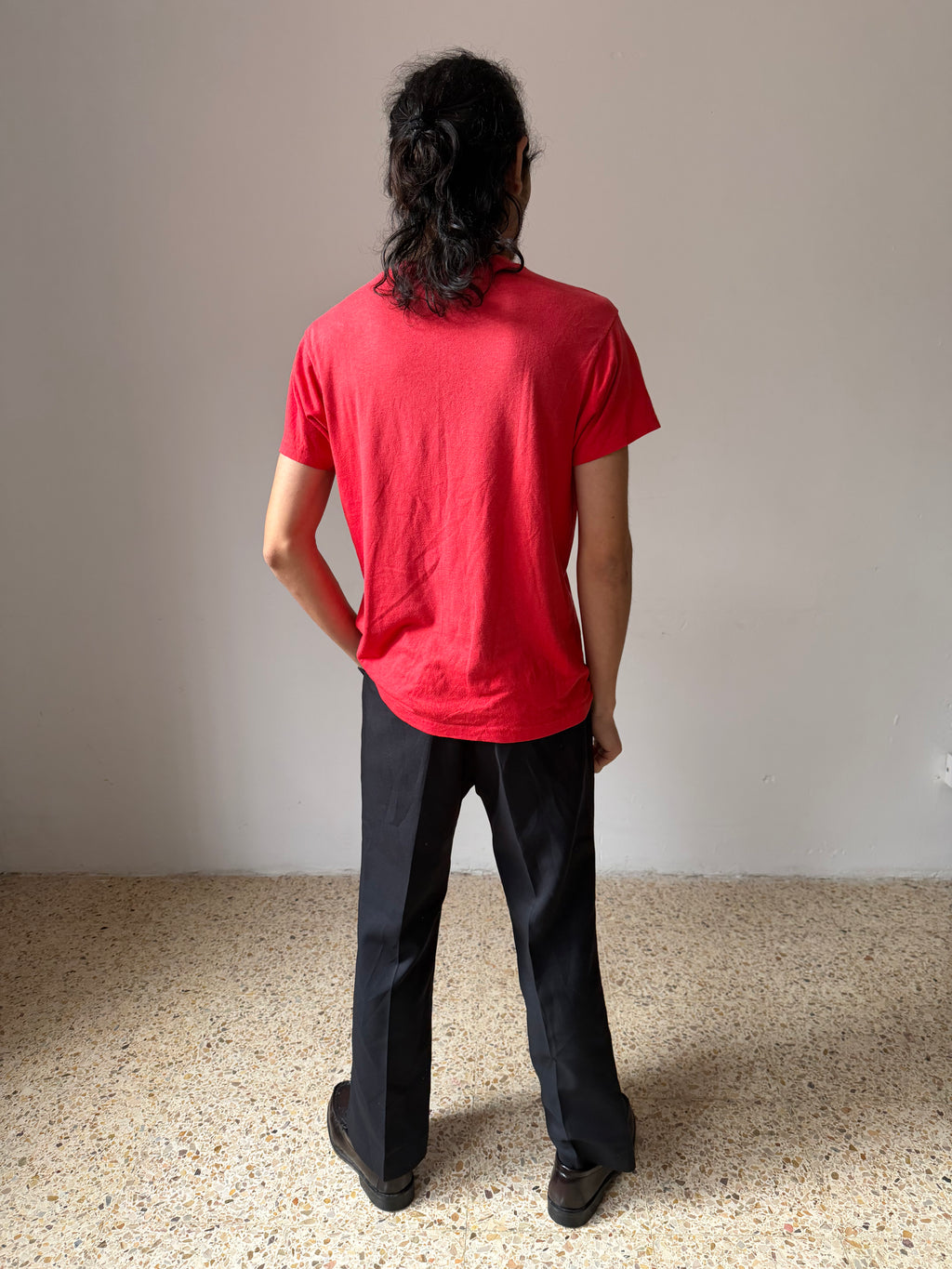 Person wearing a usmc red t-shirt and black pants standing with their back to the camera on a speckled floor.
